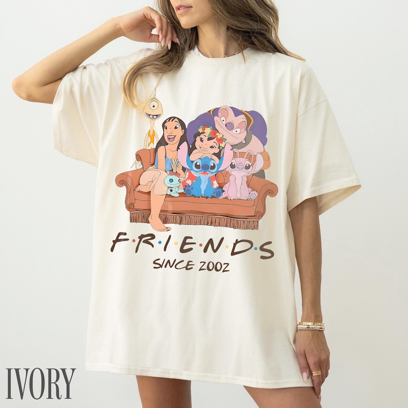 May include: Ivory-coloured t-shirt with a graphic of Lilo & Stitch characters on a brown sofa. The word "FRIENDS" is printed above "SINCE 2002" in black. The shirt has a loose fit. The word "IVORY" is printed at the bottom.