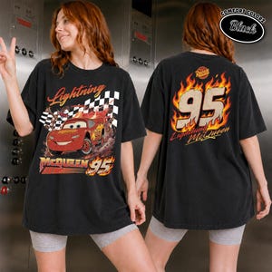 May include: Black t-shirt featuring Lightning McQueen from the Cars movie. The front graphic shows McQueen racing with the text "Lightning McQueen 95". The back displays "95" in flames with "Lightning McQueen" below. The shirt is labeled "Comfort Colors".