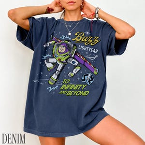 Pode incluir: Uma camiseta azul marinho com um desenho de Buzz Lightyear. O design inclui o texto "Buzz Lightyear" e "To Infinity and Beyond" em amarelo e branco. A camiseta tem um corte folgado.