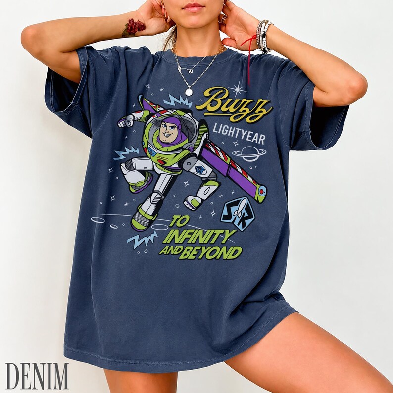 Pode incluir: Uma camiseta azul marinho com um desenho de Buzz Lightyear. O design inclui o texto "Buzz Lightyear" e "To Infinity and Beyond" em amarelo e branco. A camiseta tem um corte folgado.