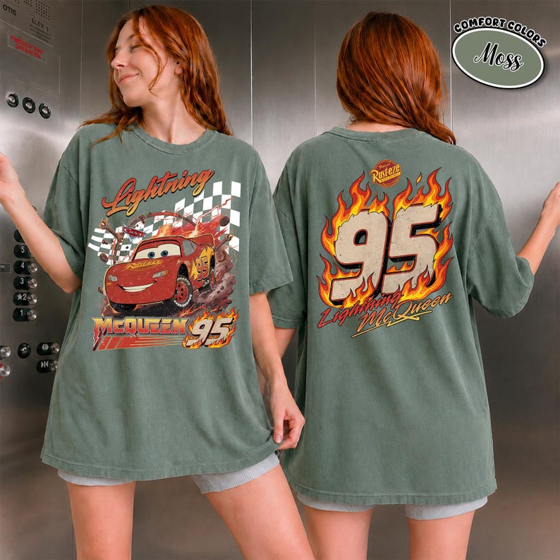 May include: A moss green t-shirt featuring Lightning McQueen from the Cars movie. The front graphic shows McQueen racing with the text "Lightning McQueen 95". The back displays "95" in flames and "Lightning McQueen".