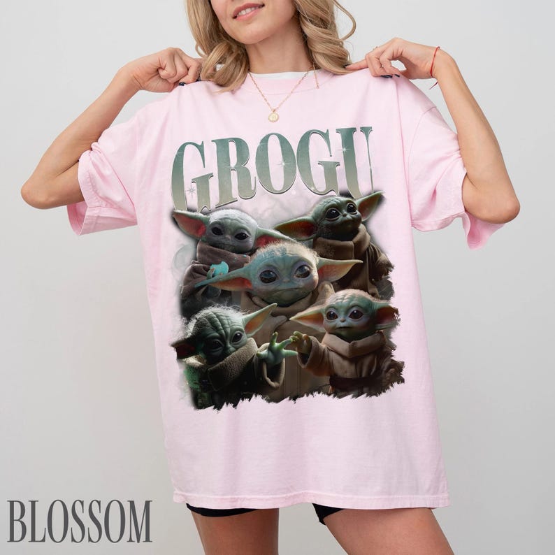 K&ouml;nnte beinhalten: Ein hellrosa T-Shirt mit dem Wort "GROGU" in einer verblassten Schriftart &uuml;ber einer Grafik von Grogu, auch bekannt als Baby Yoda, aus der Star Wars-Serie. Die Grafik zeigt Grogu in verschiedenen Posen. Das Wort "BLOSSOM" ist unten aufgedruckt.