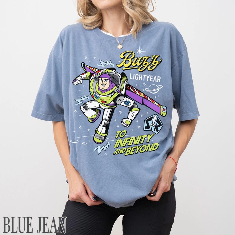 Pode incluir: Camiseta azul clara com um desenho do Buzz Lightyear voando. O design inclui o texto "Buzz Lightyear" e "To Infinity and Beyond". A camiseta tem um corte folgado.