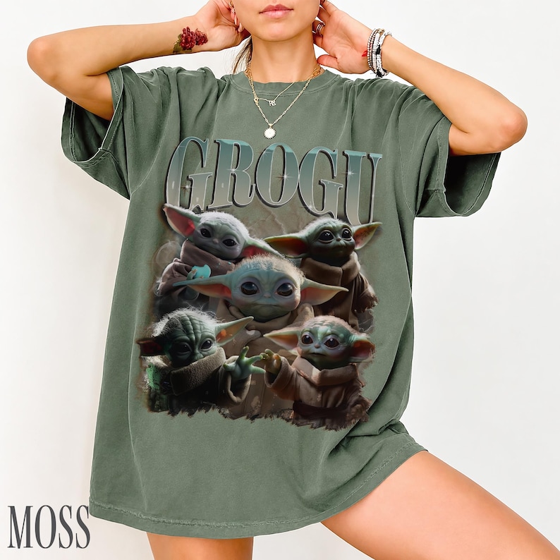 K&ouml;nnte beinhalten: Moosgr&uuml;nes T-Shirt mit dem Wort "GROGU" &uuml;ber einer Grafik von Grogu aus The Mandalorian. Die Grafik zeigt Grogu in verschiedenen Posen. Das Wort "MOSS" ist unten links aufgedruckt.