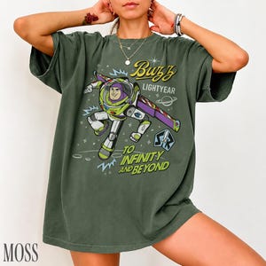Pode incluir: T-shirt verde musgo com um gr&aacute;fico de Buzz Lightyear de Toy Story. O design inclui o texto "Buzz Lightyear" e "To Infinity and Beyond". A camisa tem um ajuste folgado.