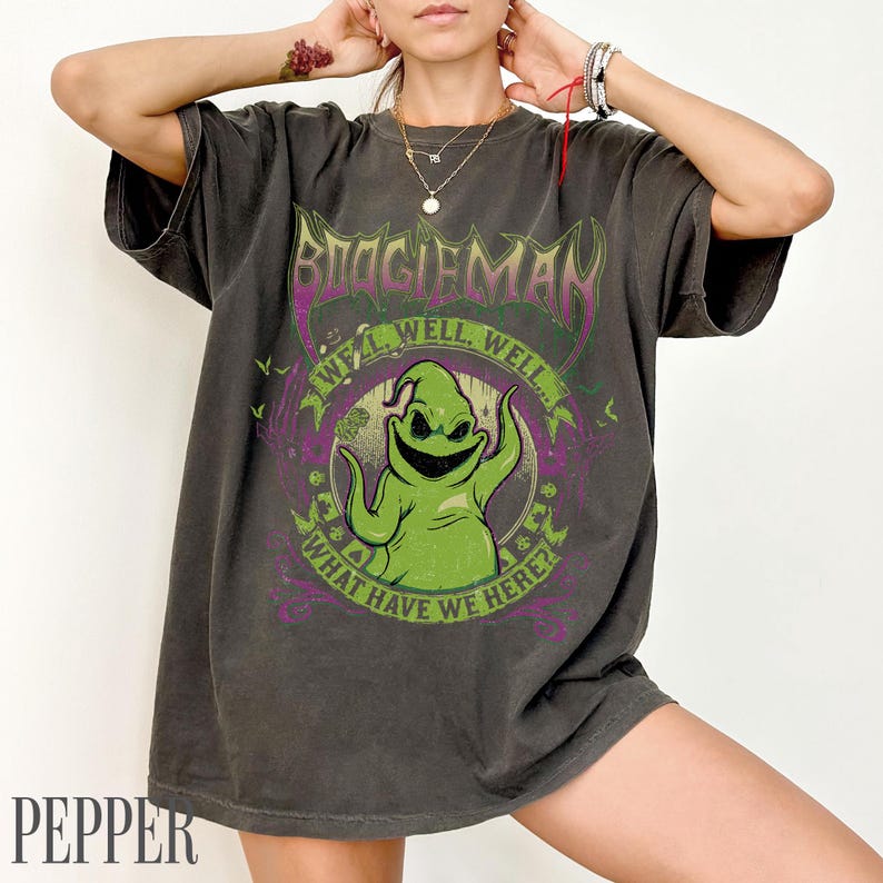 May include: Dark grey t-shirt with a green Oogie Boogie character design from The Nightmare Before Christmas. The design includes the text "BOOGIEMAN", "WELL, WELL, WELL...", and "WHAT HAVE WE HERE?" in purple and green.
