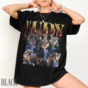 May include: Black t-shirt featuring a graphic of Judy Hopps from Zootopia. The design includes the name "JUDY" in gold lettering and images of Judy Hopps and other characters. The word "BLACK" is printed at the bottom.