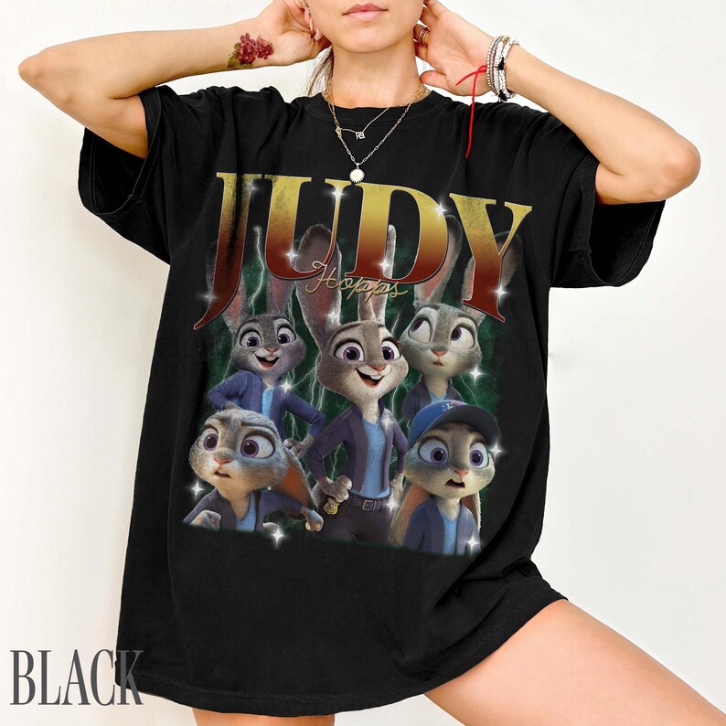 May include: Black t-shirt featuring a graphic of Judy Hopps from Zootopia. The design includes the name "JUDY" in gold lettering and images of Judy Hopps and other characters. The word "BLACK" is printed at the bottom.
