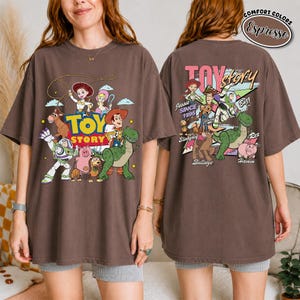 K&ouml;nnte beinhalten: Espressofarbenes T-Shirt mit einer farbenfrohen Grafik von Toy Story-Charakteren. Das Frontdesign zeigt Woody, Buzz Lightyear und Jessie. Das R&uuml;ckendesign zeigt den Text "Toy Story" und zus&auml;tzliche Charaktere. Das Shirt ist von der Marke Comfort Colors.