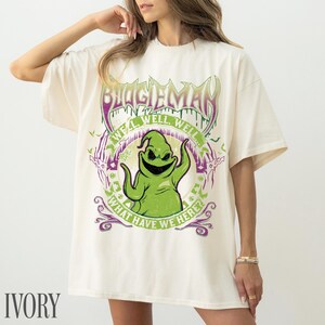 May include: Ivory-coloured t-shirt with a graphic of Oogie Boogie from The Nightmare Before Christmas. The design includes the text "BOOGIEMAN" and "WE'LL WELL WELL! WHAT HAVE WE HERE?" in green and purple.