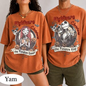 Puede incluir: Dos camisetas de color naranja quemado con gr&aacute;ficos de Nightmare Before Christmas. La camiseta izquierda muestra a Sally con el texto The Pumpkin Queen, mientras que la derecha muestra a Jack Skellington con el texto The Pumpkin King. Ambas incluyen marcos circulares, murci&eacute;lagos y calabazas.