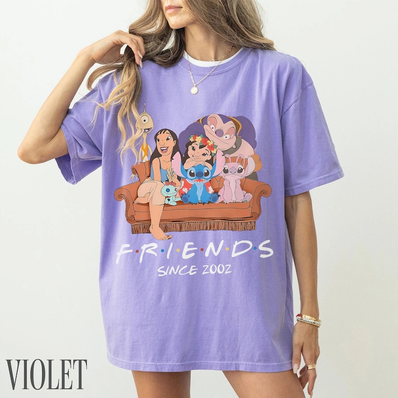 May include: Lilac t-shirt with a cartoon image of Lilo & Stitch characters on a brown sofa. The word "FRIENDS" is above "SINCE 2002" in white. The word "VIOLET" is printed in white at the bottom. The t-shirt is a relaxed fit.