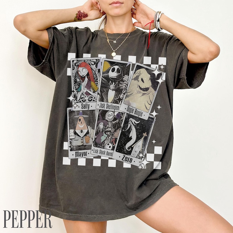 May include: Dark gray t-shirt featuring playing card designs with characters from "The Nightmare Before Christmas." The cards include Sally, Jack Skellington, Oogie Boogie, Mayor, Lock Shock Barrel, and Zero. The word "PEPPER" is at the bottom.