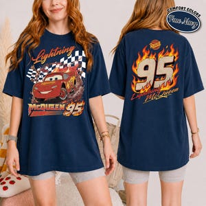 May include: Navy blue t-shirt featuring Lightning McQueen from the movie Cars. The front graphic shows McQueen racing with a checkered flag and the text "Lightning McQueen 95." The back displays "95" in flames with "Lightning McQueen" below.