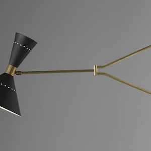 Peut inclure: Applique murale noire et laiton de style moderne du milieu du siècle. Elle présente deux abat-jours coniques noirs avec de petits détails de points blancs, reliés par un bras et une plaque de montage en laiton.