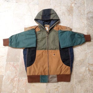 May include: A color-blocked hooded jacket featuring a full-length front zipper, brown ribbed cuffs and hem, and a Carhartt logo patch on the chest. The garment is constructed from panels of olive green, tan, black, and dark teal fabric throughout.