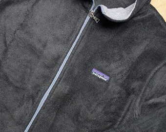 May include: A black fleece jacket with a full-length front zipper, a high collar, and a light gray interior lining. The jacket features a Patagonia brand patch on the left chest and a matching brand label inside the collar with the size L.