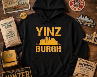 May include: A black hooded sweatshirt featuring a yellow graphic print on the chest. The text reads YINZ BURGH above and below a stylized yellow silhouette of the Pittsburgh city skyline. The hoodie has long sleeves and a front kangaroo pocket.