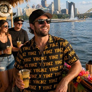 以下が含まれることがあります： YINZという文字が黄色で繰り返しプリントされた、黒の半袖ボタンダウンシャツ。クラシックな襟とフロントボタン留めが特徴で、屋外での着用に適した軽量な生地で作られています。