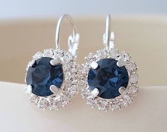 May include: A pair of silver hoop earrings with a dark blue gemstone surrounded by a halo of smaller clear gemstones.
