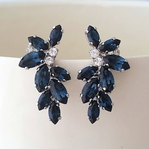 Puede incluir: Un par de pendientes de plata con un racimo de cristales de color azul oscuro en forma de marquesa. Los cristales están dispuestos en forma de cascada, creando un aspecto delicado y elegante.