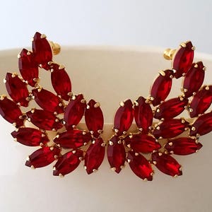 May include: A pair of gold earrings with red marquise-shaped crystals arranged in a wing-like design.