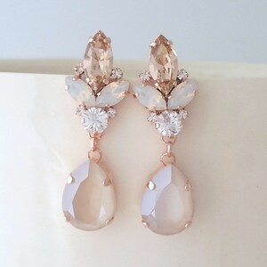 Puede incluir: Pendientes colgantes de oro rosa con un cristal en forma de lágrima y un racimo de cristales más pequeños en champán y blanco.
