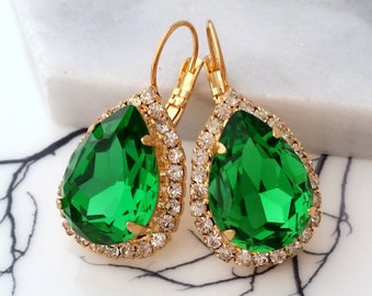 May include: A pair of gold dangle earrings with emerald green teardrop-shaped stones surrounded by a halo of clear rhinestones.