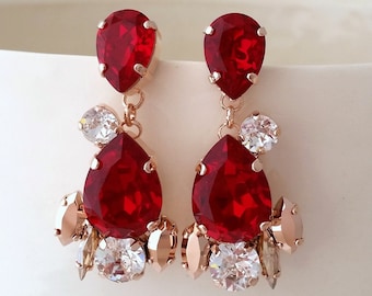 May include: A pair of dangle earrings with red and clear crystal stones. The earrings have a rose gold finish.