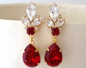 May include: Gold dangle earrings with a cluster of clear rhinestones and a teardrop-shaped red gemstone.