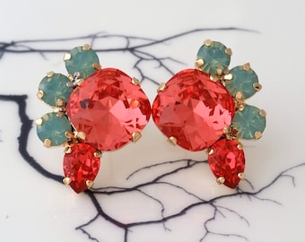 May include: A pair of coral red and light green crystal earrings. The earrings are made of faceted crystals and have a cluster design.