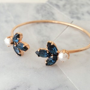 May include: Gold bangle bracelet with two blue crystal flower accents and white pearl accents.