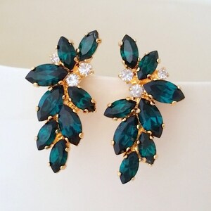 May include: A pair of gold earrings with emerald green marquise-shaped crystals. The crystals are arranged in a cascading pattern, creating a delicate and elegant look.