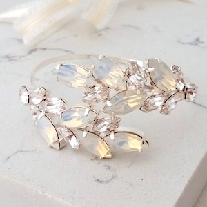 May include: A silver bracelet with a delicate design featuring a cluster of white opal and clear crystal stones. The bracelet is open and adjustable.