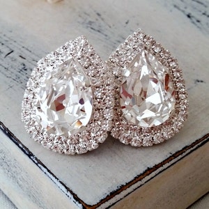 May include: A pair of silver teardrop-shaped earrings with large clear crystal stones surrounded by smaller clear crystals.