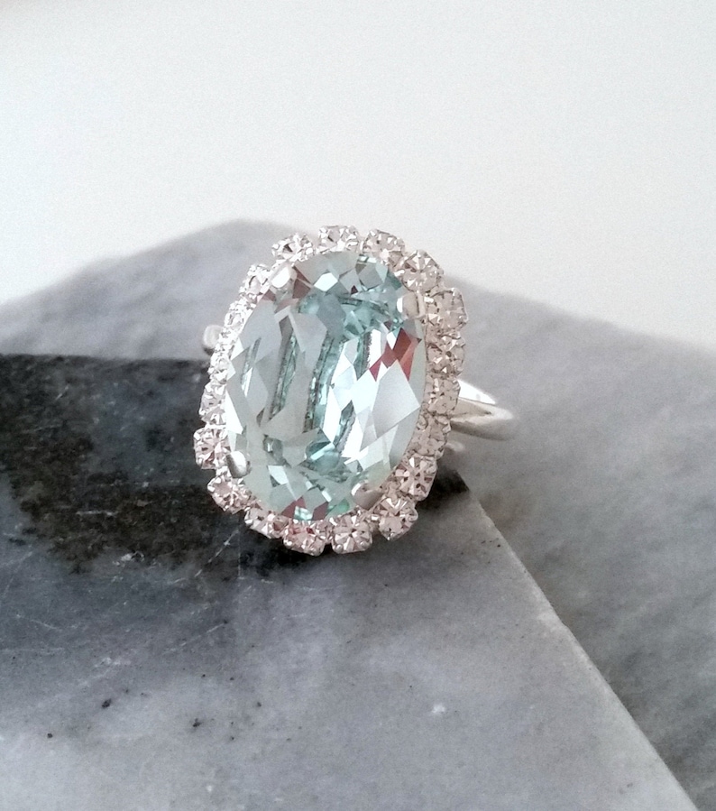 May include: A silver ring with a large oval aquamarine gemstone surrounded by a halo of smaller diamonds.