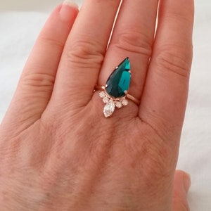May include: A teardrop-shaped emerald green ring with a silver band and a cluster of smaller clear stones.