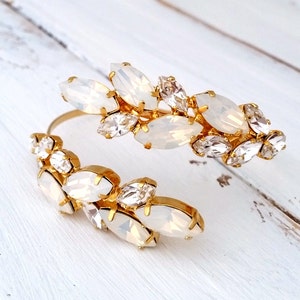 May include: A gold cuff bracelet with a cluster of white and clear crystal stones. The stones are arranged in a floral pattern.