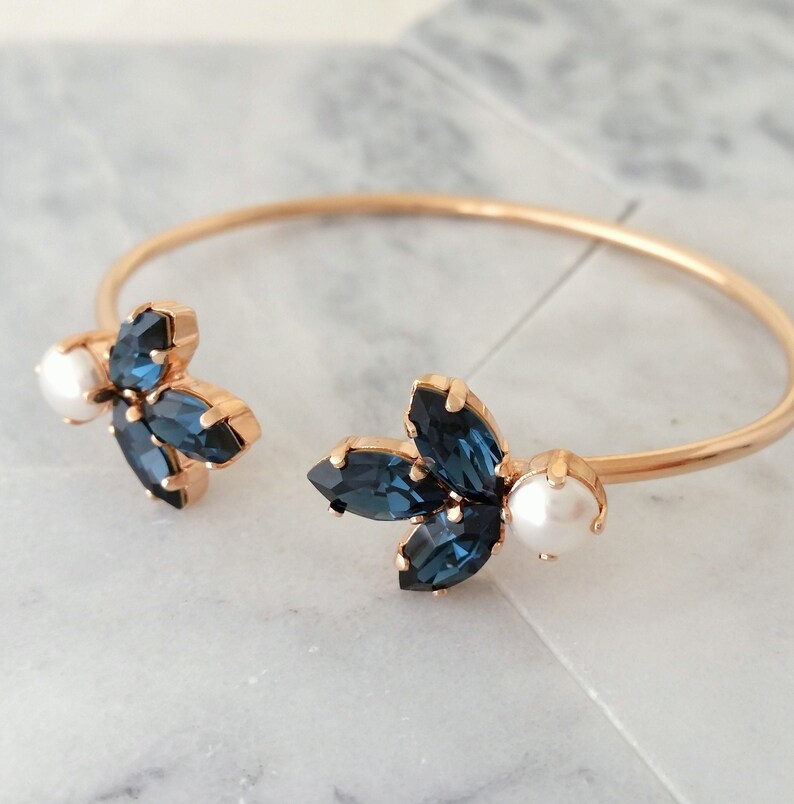 May include: Gold bangle bracelet with two blue crystal flower accents and white pearl accents.