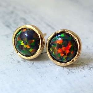 May include: A pair of gold stud earrings with black opal gemstones. The opals have a rainbow of colors, including green, red, and orange.