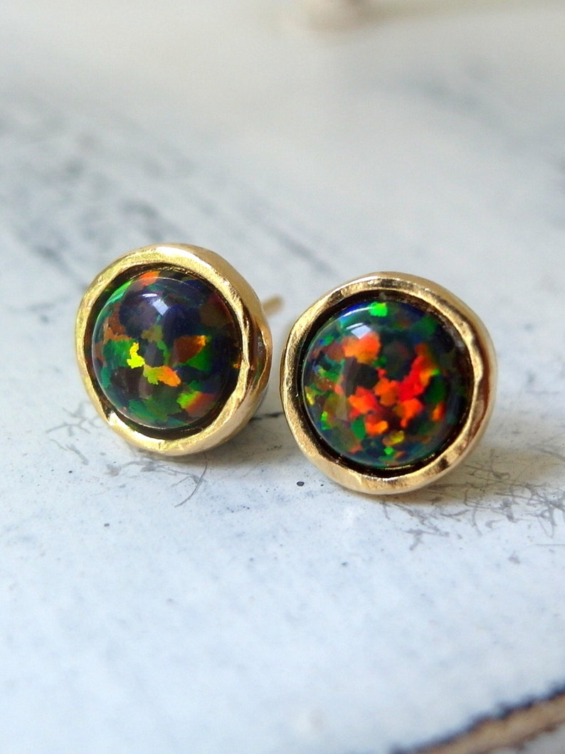 May include: A pair of gold stud earrings with black opal gemstones. The opals have a rainbow of colors, including green, red, and orange.