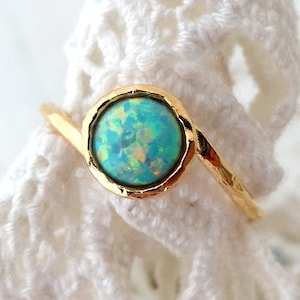 May include: A gold ring with a light blue opal gemstone. The ring has a hammered finish and a simple design.