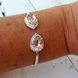 May include: A silver bangle bracelet with two pear-shaped pink crystals set in a silver halo of smaller crystals.