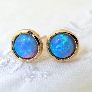 May include: A pair of gold stud earrings with blue opal gemstones. The earrings have a hammered texture and a round shape.