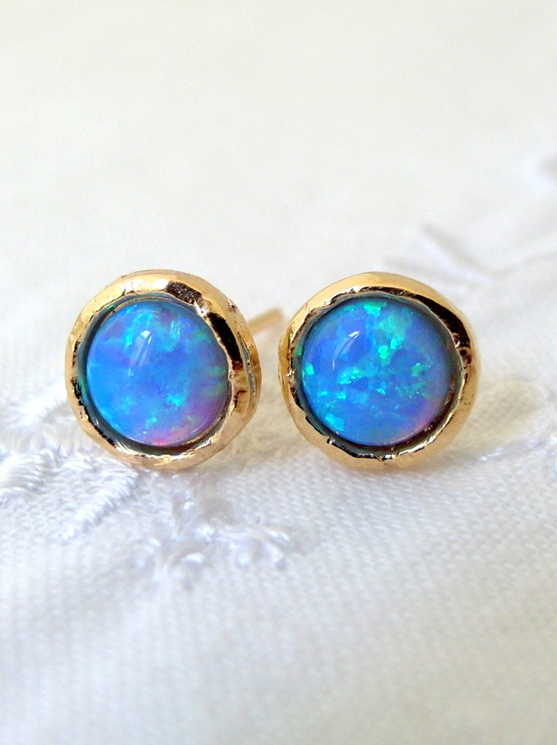 May include: A pair of gold stud earrings with blue opal gemstones. The earrings have a hammered texture and a round shape.