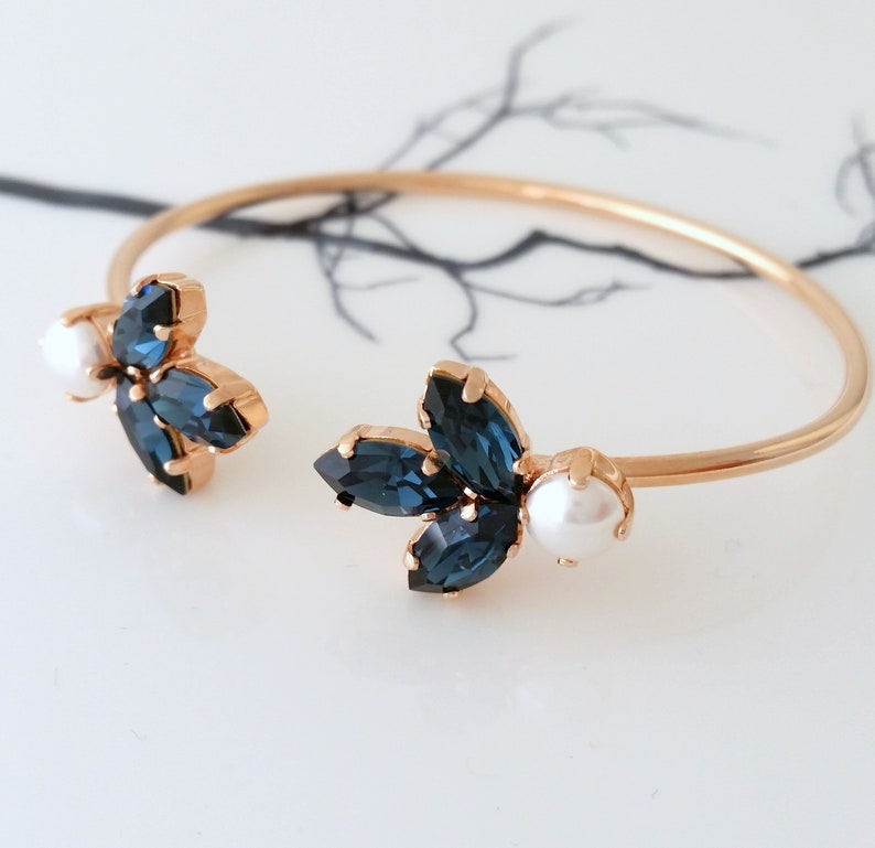 May include: A gold bangle bracelet with two blue crystal flower accents and pearl embellishments.