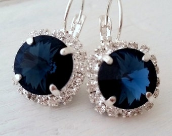 May include: A pair of silver dangle earrings with a large, dark blue gemstone surrounded by a halo of smaller clear rhinestones.