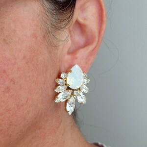 May include: Gold earrings with a large white opal teardrop stone surrounded by smaller clear crystals.