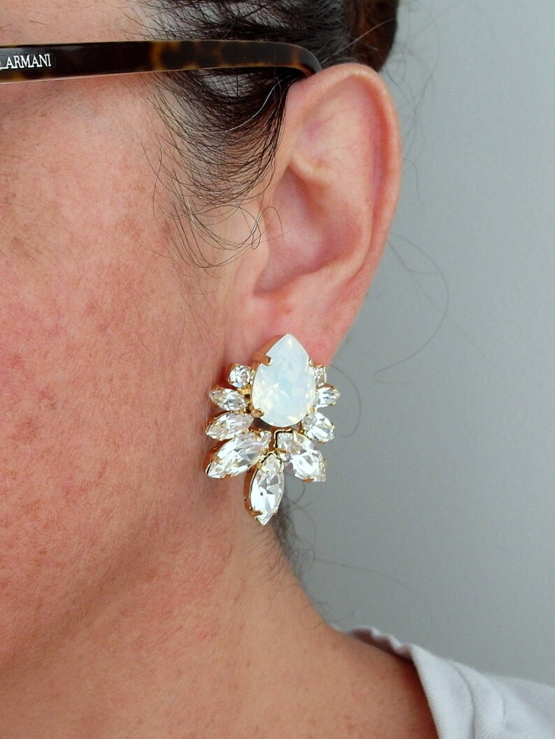 May include: Gold earrings with a large white opal teardrop stone surrounded by smaller clear crystals.