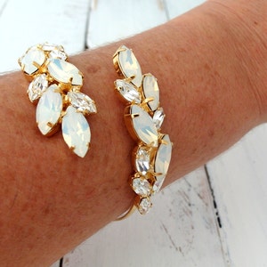 May include: A gold cuff bracelet with a design of white opal-like stones arranged in a leaf pattern.